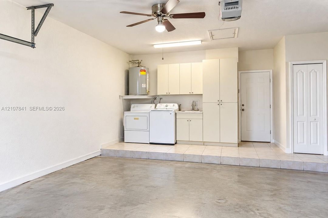 Garage area featuring a concrete floor, tile-surfaced elevated workspace, built-in cabinetry with integrated sink, ceiling fan, and laundry hookups