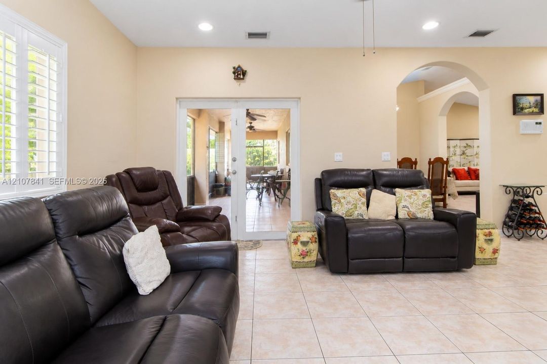 Neutral interior featuring light tile flooring, recessed lighting, plantation shutters, and an arched entryway with double-door access to an exterior screened enclosure