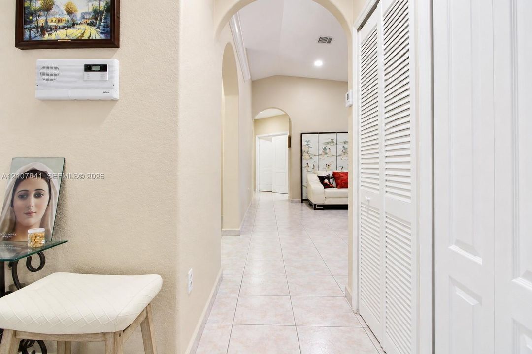 Hallway featuring arched architectural openings, neutral ceramic tile flooring, and white louvered-style closet doors