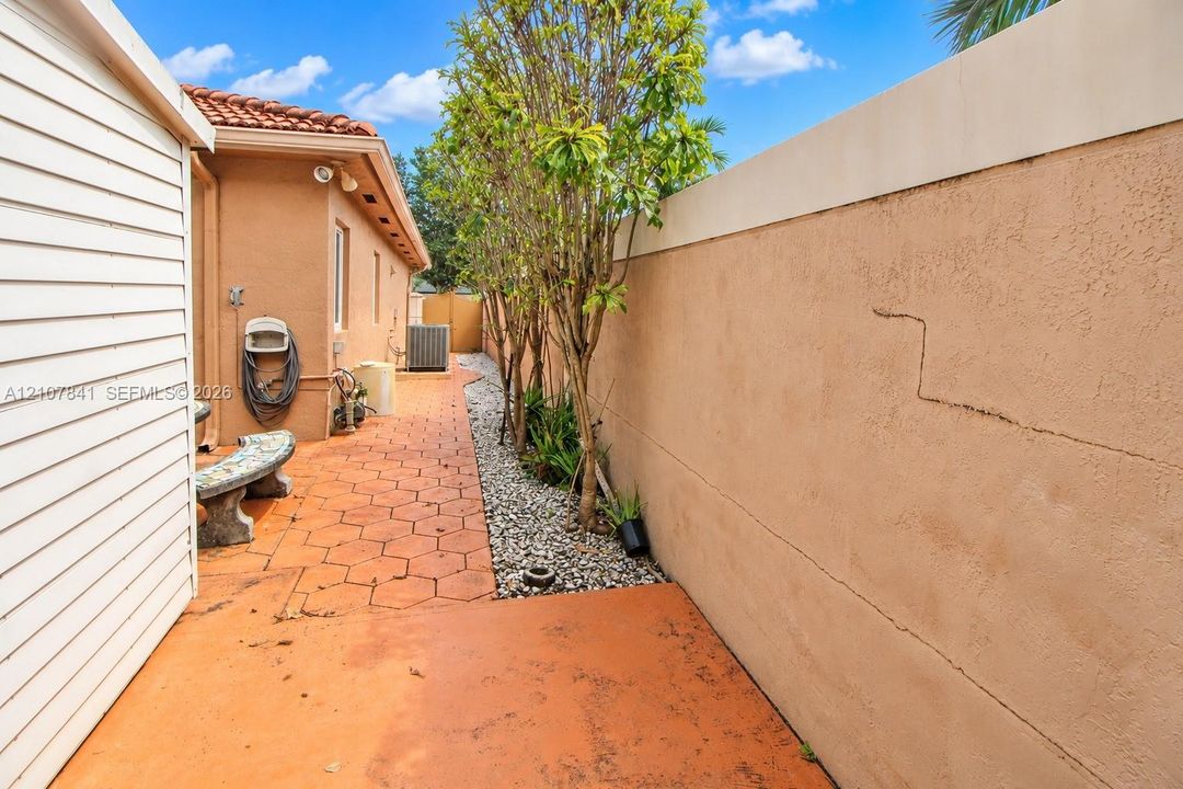 Side patio featuring hexagonal pavers, a perimeter masonry wall, stone ground cover, and mature landscape plantings