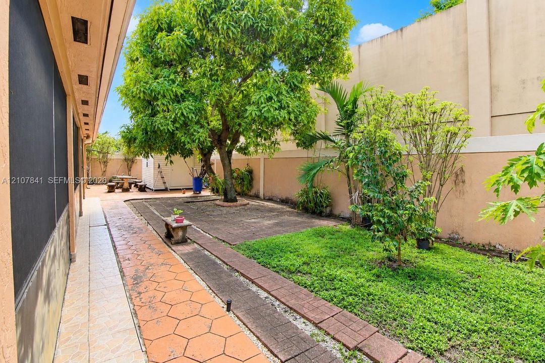 Private backyard featuring a paved patio, perimeter masonry wall, mature trees, and landscaped lawn area