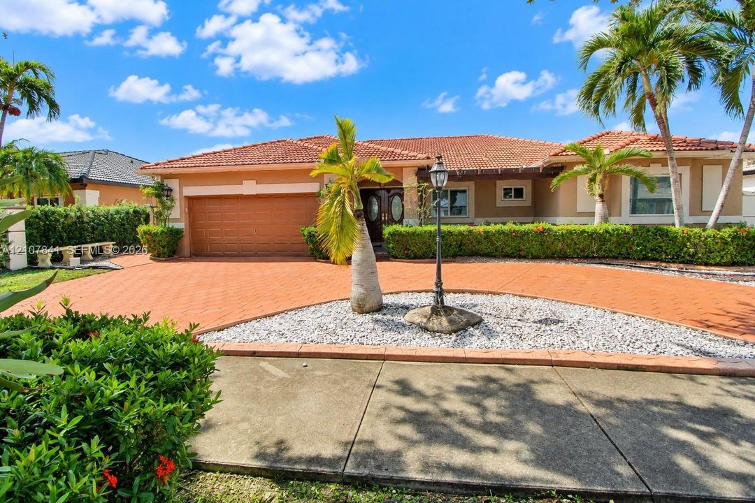Single-story exterior featuring a clay tile roof, paver driveway, built-in post lamp, multi-car garage, and established landscaping
