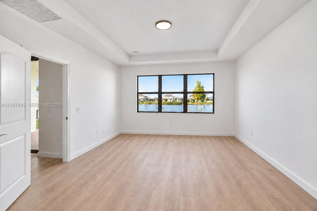 Room featuring wood-finish flooring, a tray ceiling, flush-mount lighting, and expansive windows with water scenery