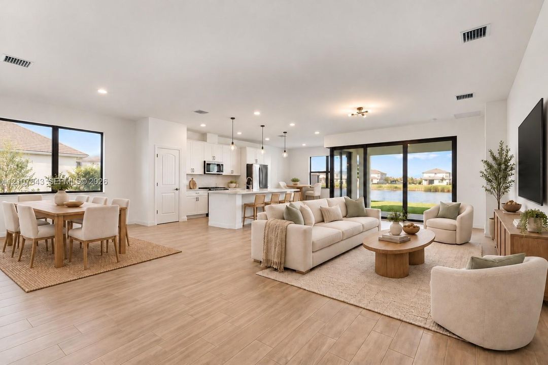 Open-concept main living area featuring wood-finish flooring, a kitchen island with stone-style countertops, recessed lighting, and large sliding glass doors providing outdoor exposure