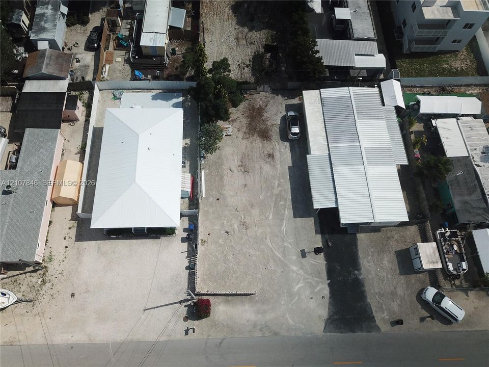 Aerial perspective of an expansive lot featuring a metal-roofed structure and a secondary building with a covered carport