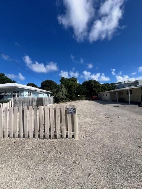 Gravel-surfaced lot featuring a wood picket fence enclosure and exterior covered structure coverage
