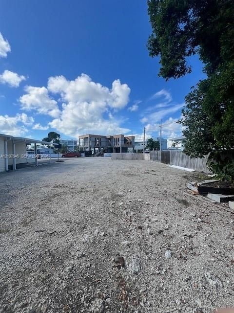 Expansive lot featuring crushed stone surfacing, perimeter wood fencing, and mature trees