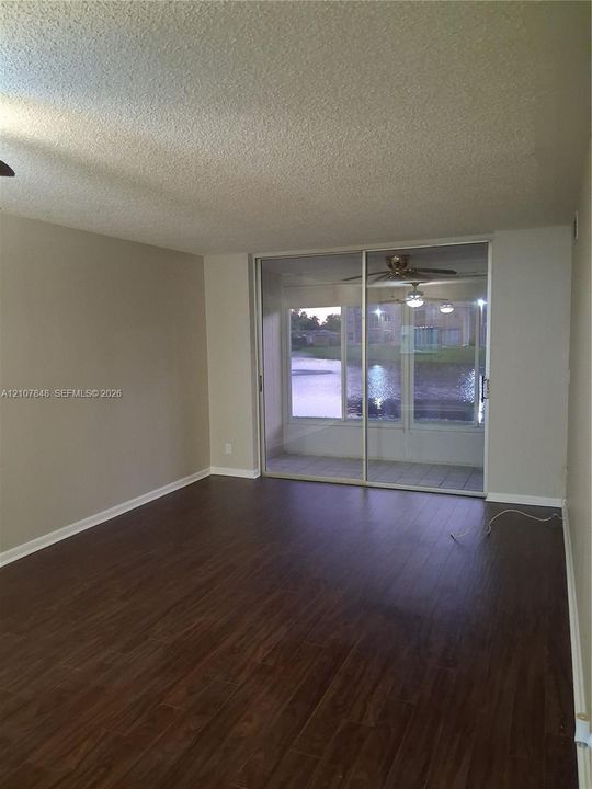 Living area featuring wood-finish flooring, textured ceiling, and floor-to-ceiling sliding glass doors opening to a screened-in lanai with water scenery
