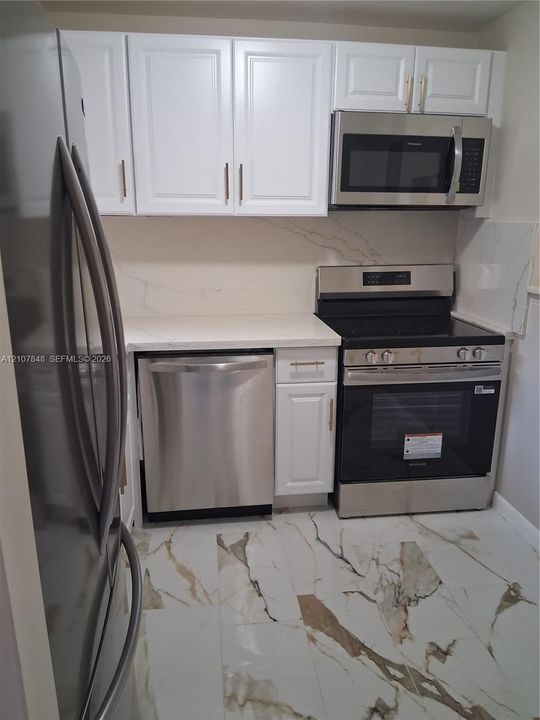 Kitchen featuring white shaker-style cabinetry, stainless steel appliances, quartz countertops, full-height stone-patterned backsplash, and large-format porcelain tile flooring