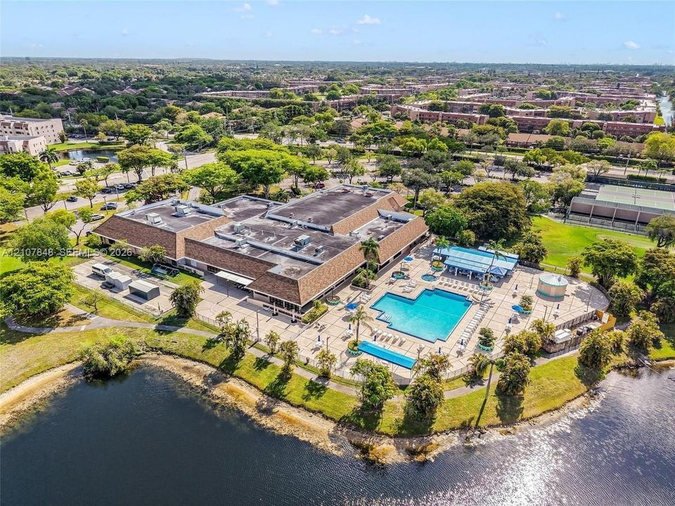 Aerial perspective featuring a multi-wing building, expansive outdoor swimming pool, paved pool deck, and direct water frontage on a lake