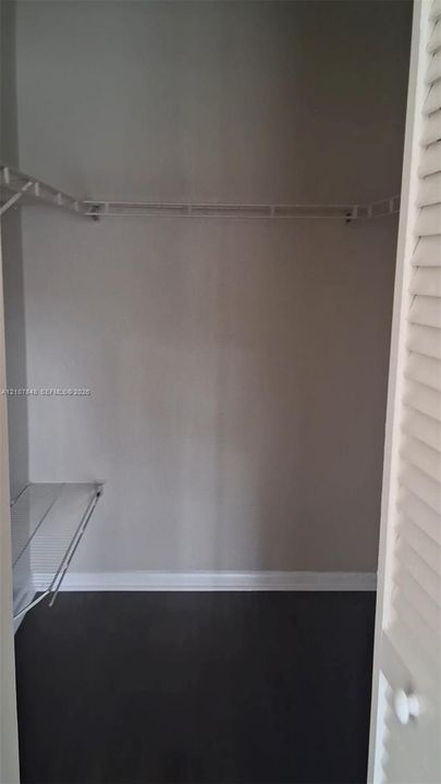 Storage area featuring dark wood-finish flooring, white louvered doors, and white wire shelving