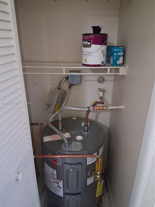 Water heater enclosure featuring a louvered door, wire shelving, and copper plumbing components