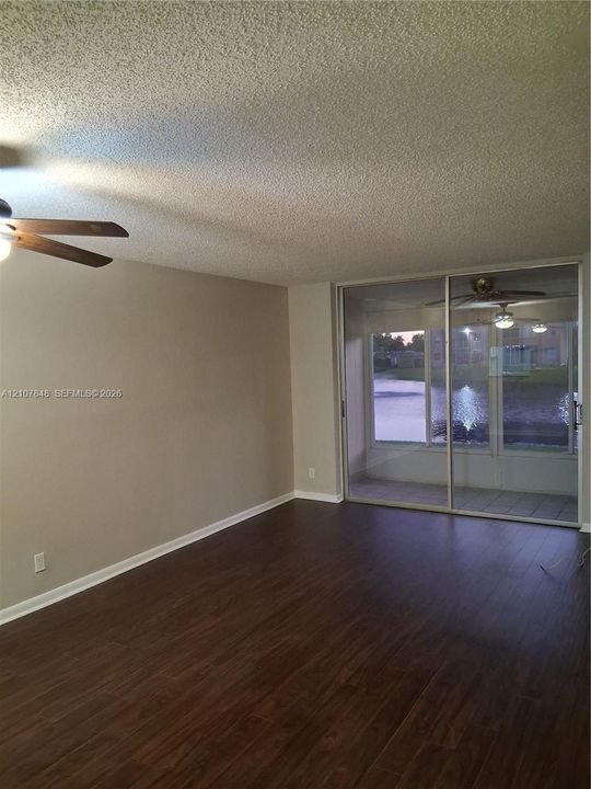 Living area featuring wood-finish flooring, textured ceiling, ceiling fan, and sliding glass doors opening to a screened enclosure
