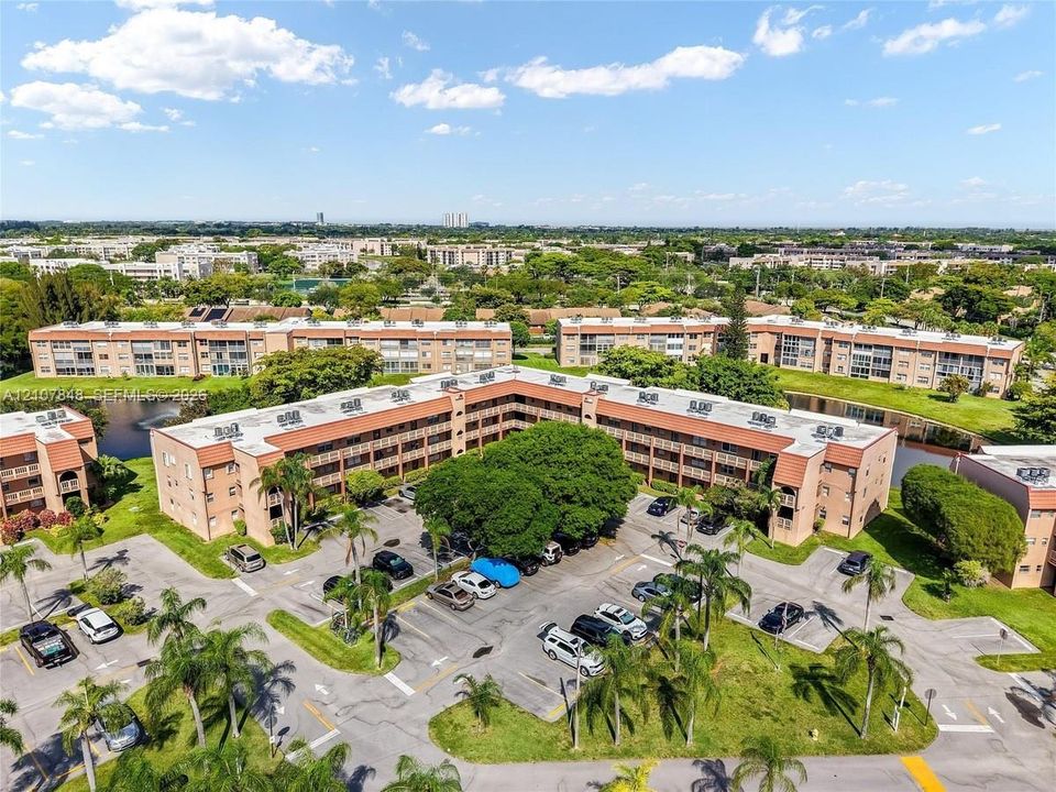Aerial perspective of a multi-story residential complex featuring brick-finished exteriors, dedicated surface parking, mature tropical landscaping, and a central water feature