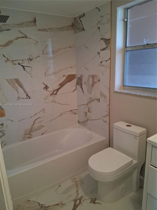 Full-height shower surround featuring large-format veined tile, integrated soaking tub, floor-to-ceiling tile flooring, and dual-flush toilet