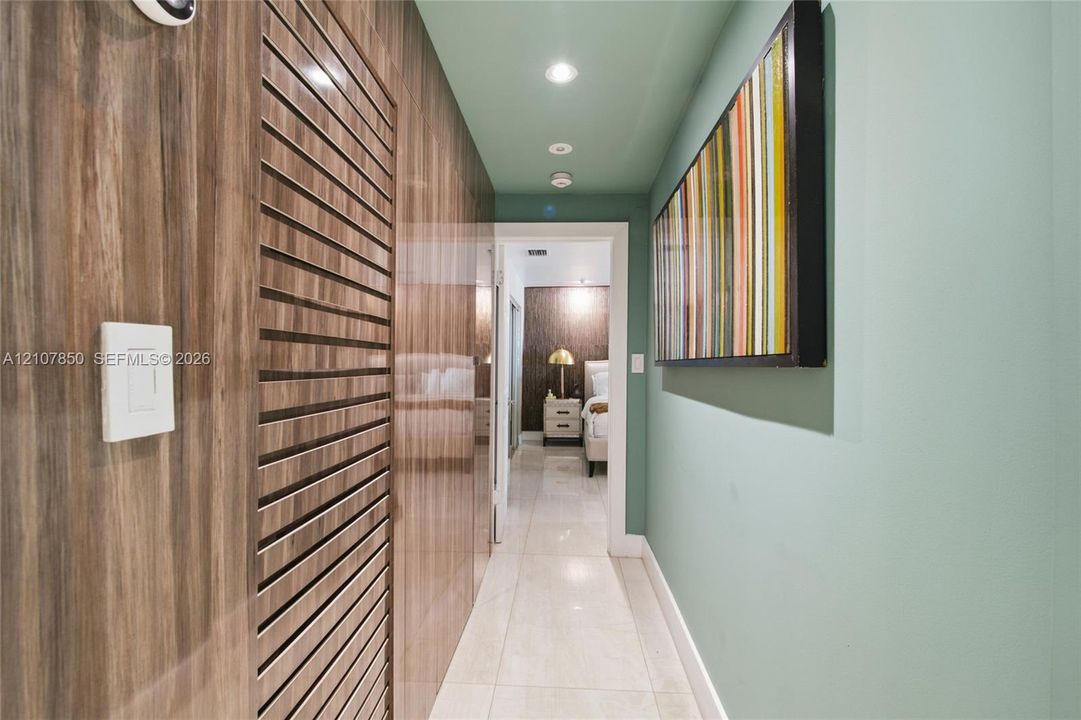 Hallway featuring polished tile flooring, vertical wood-panel wall treatments, louvered built-in cabinet doors, and recessed ceiling lighting