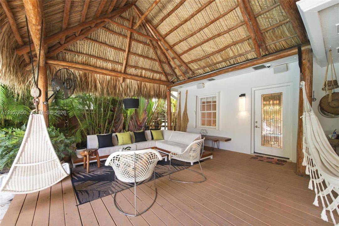 Covered patio featuring a thatched gable roof with exposed log support beams, composite decking, and a wall-mounted light fixture