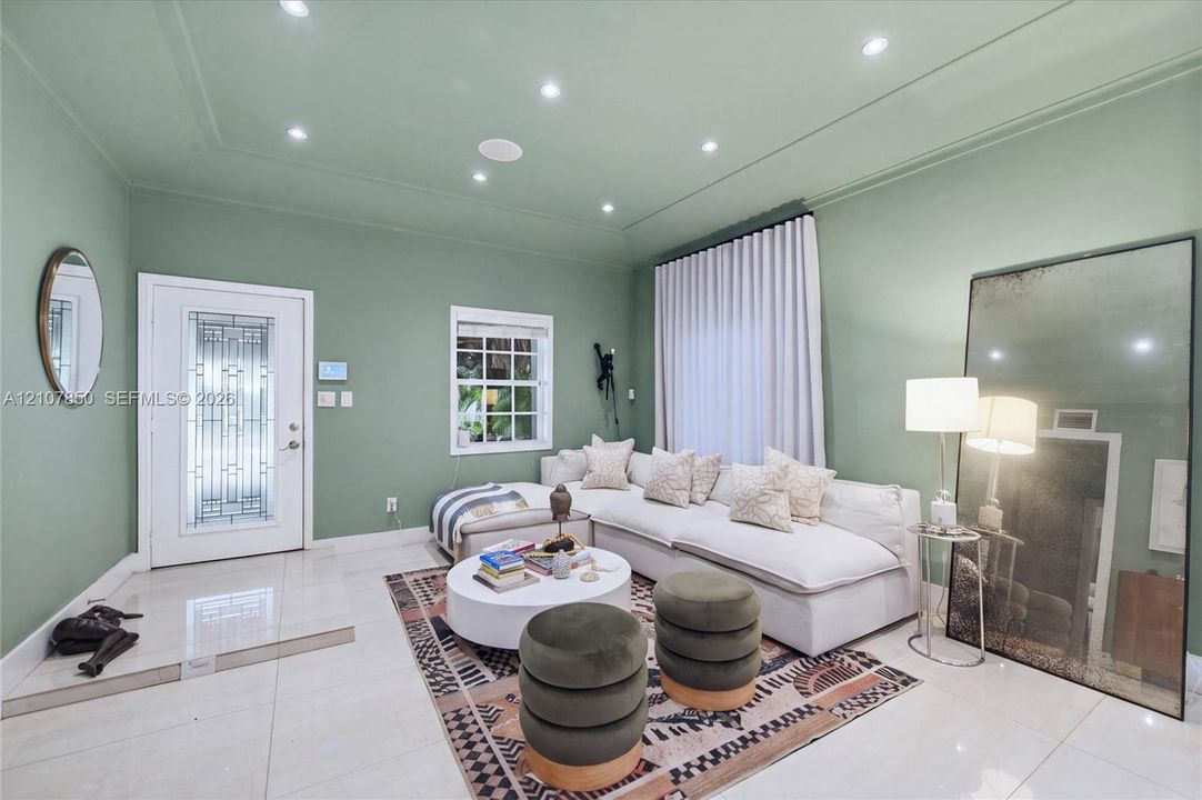 Living area featuring large-format tile flooring, tray ceiling, recessed lighting, and an exterior door with integrated decorative glass panels