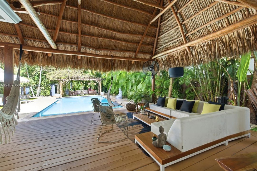 Open-air pavilion featuring a thatched roof, wood-finish decking, and a built-in wall-mounted fan, overlooking an in-ground swimming pool