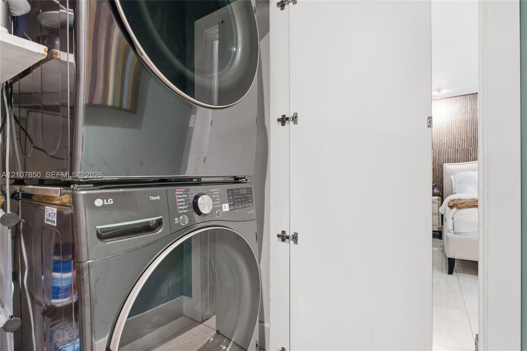 Stacked stainless steel laundry appliances housed within a white cabinetry enclosure