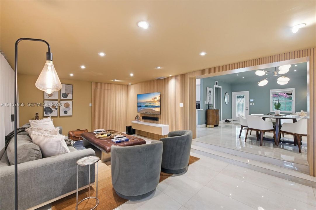 Living space featuring vertical wood slat paneling, recessed lighting, and large-format polished tile flooring