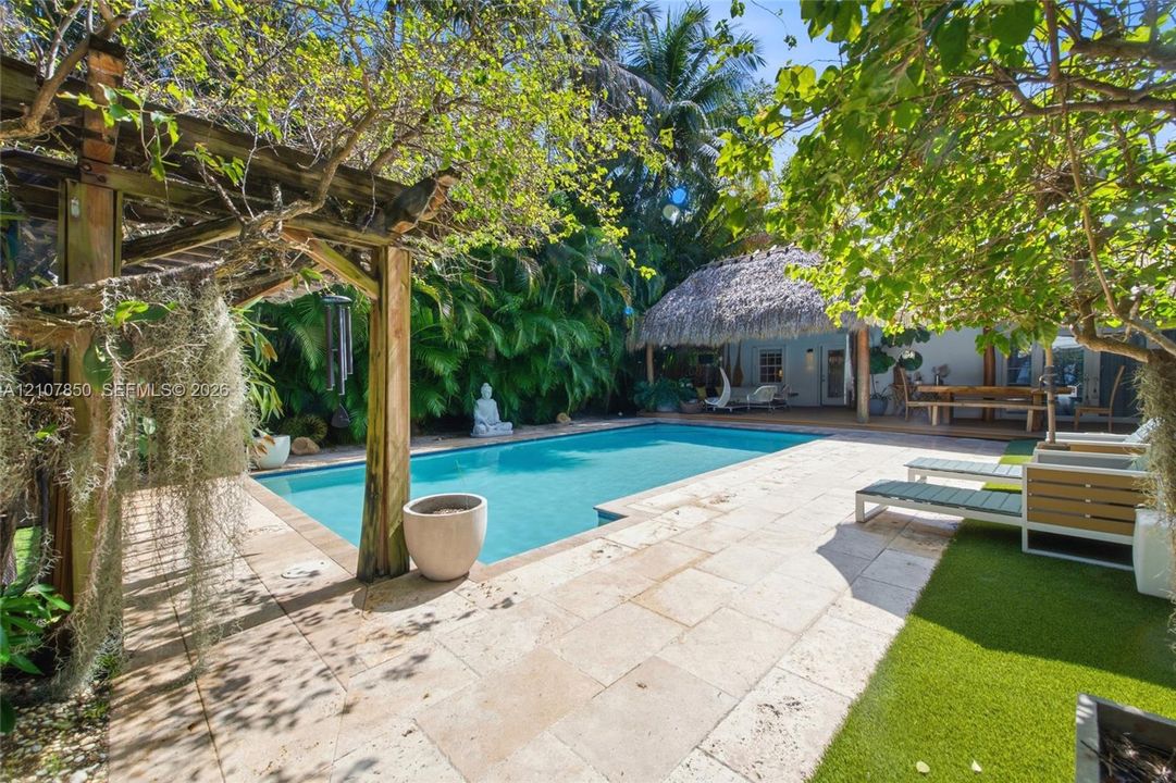 In-ground swimming pool featuring a stone-paver deck, custom wood pergola, and a thatched-roof cabana structure