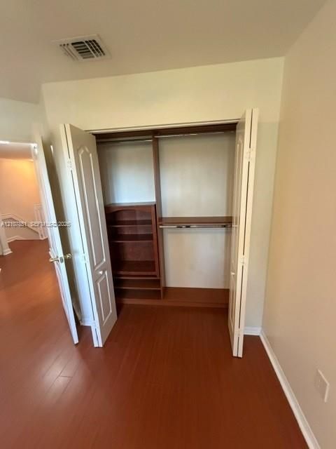 Closet featuring white bi-fold doors, built-in wooden shelving, and a metal hanging rod, complemented by wood-finish flooring
