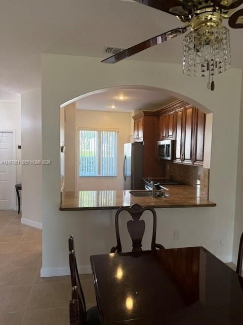 Kitchen featuring an arched pass-through opening, stone-surface breakfast bar, wood-finish cabinetry, stainless steel appliances, and a decorative ceiling fan with crystal-style accents