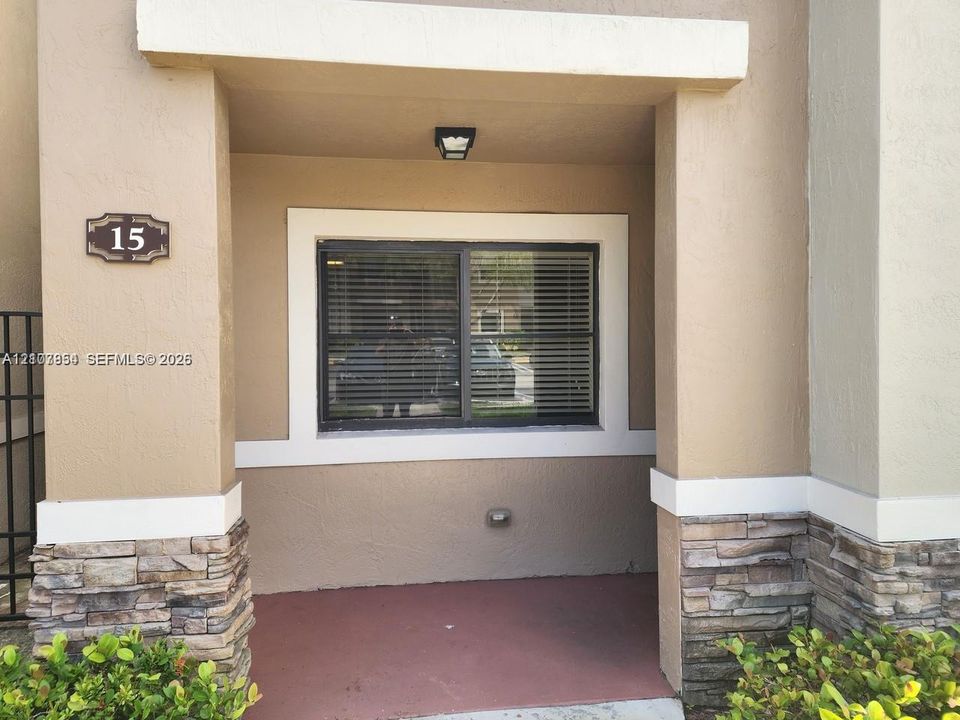 Covered entryway featuring stucco walls with stone veneer accents, a sliding window with contrasting trim, and a surface-mounted exterior light fixture