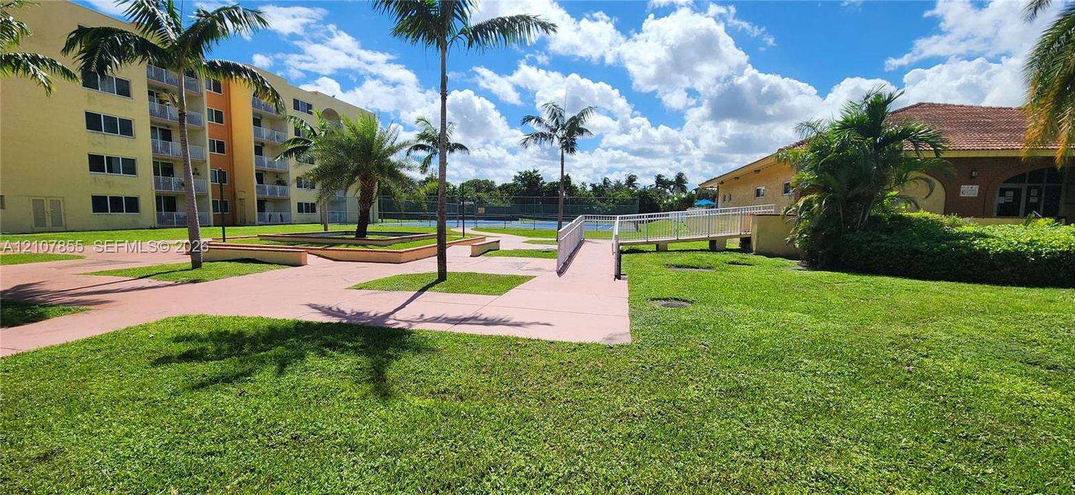 Common grounds featuring manicured lawns, mature palm trees, paved walkways, and recreational court facilities