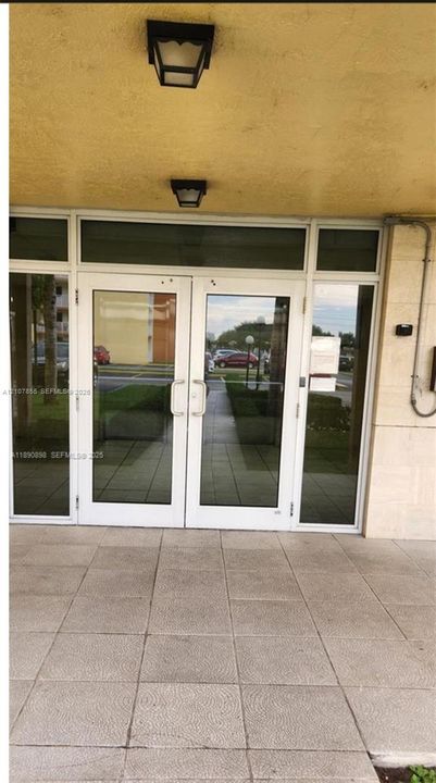 Double-glass entry doors with metal handles, sidelights, transom windows, and dual exterior light fixtures on a covered tiled entryway