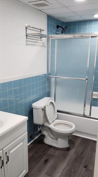 Bathroom featuring wood-finish flooring, blue tile shower surround, sliding glass shower door, and wall-mounted metal towel rack