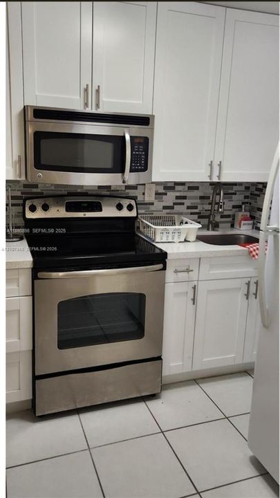 Kitchen featuring white shaker-style cabinetry, stainless steel appliances, a stone-surface countertop, tile backsplash, and a sink with a gooseneck faucet