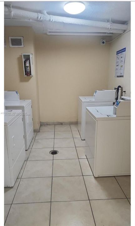Laundry area featuring ceramic tile flooring, ceiling-mounted lighting, and multiple washer and dryer units