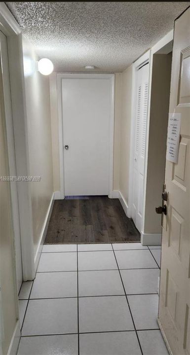 Interior hallway featuring large-format ceramic tile flooring, wood-finish flooring accents, and a paneled closet door with louvered venting
