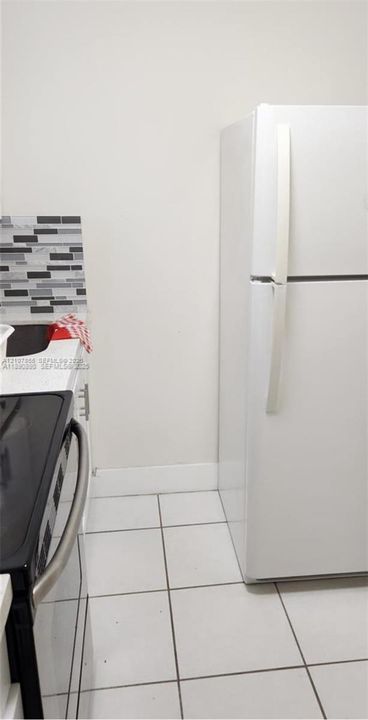 White top-freezer refrigerator, white ceramic tile flooring, and multi-tone mosaic tile backsplash