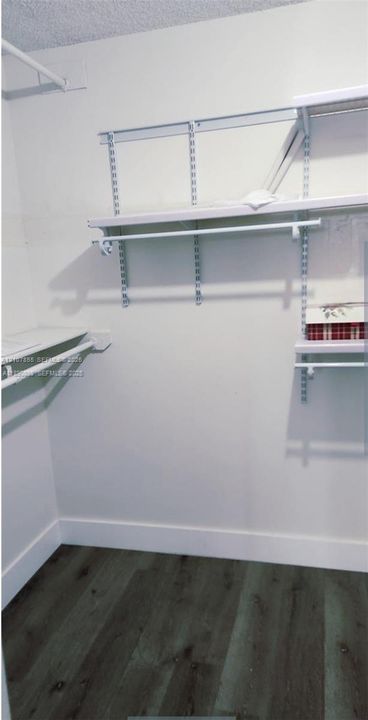 Walk-in closet featuring wood-finish flooring and adjustable white wire shelving units with integrated hanging rods