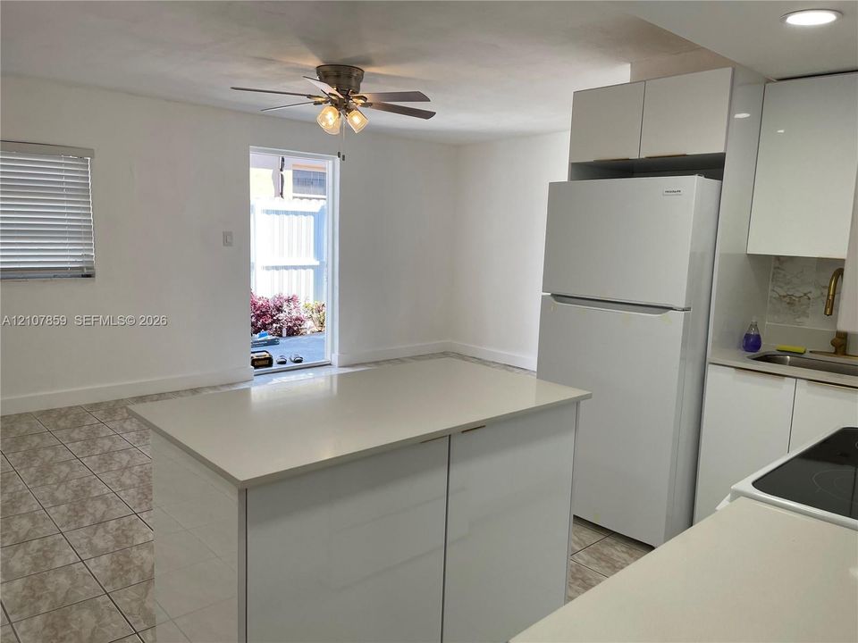 Kitchen featuring a central island with a solid-surface countertop, high-gloss white cabinetry, white appliances, and ceramic tile flooring