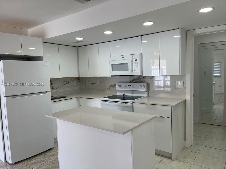 Kitchen featuring high-gloss white cabinetry, solid surface countertops, a full-height decorative backsplash, integrated recessed lighting, and a center island