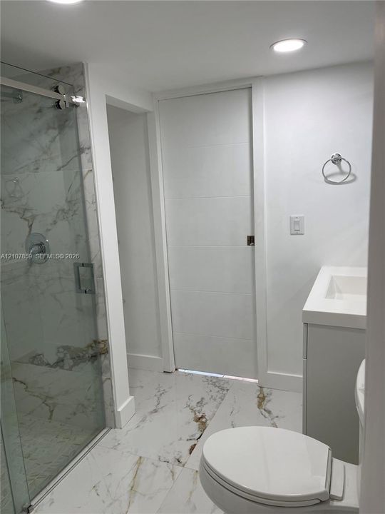 Bathroom featuring a walk-in shower with glass enclosure, large-format stone-finish tile flooring, white vanity with integrated sink, and recessed lighting