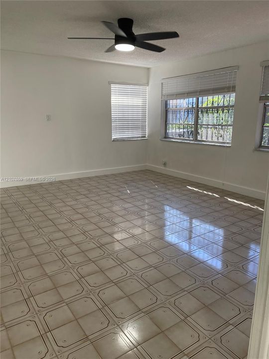 Neutral-toned ceramic tile flooring, matte black ceiling fan with integrated lighting, and multi-pane windows featuring horizontal blinds