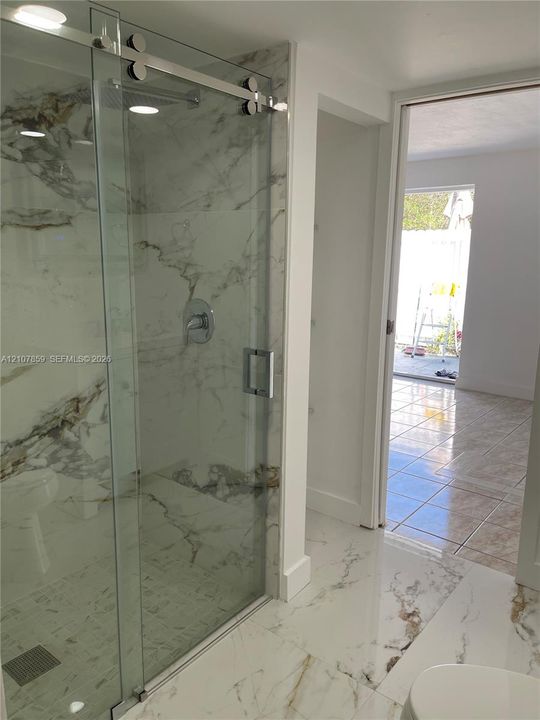 Walk-in shower featuring large-format stone-finish tile, glass sliding barn-style door, and polished chrome hardware, complemented by stone-finish tile flooring