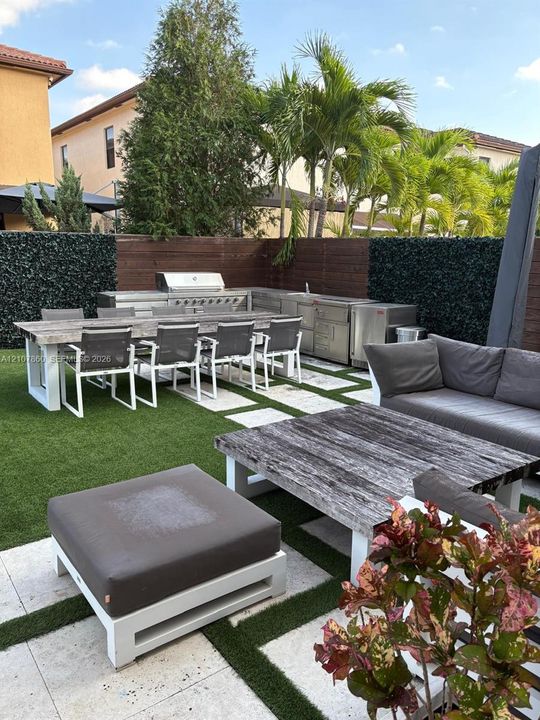 Outdoor kitchen featuring stainless steel appliances and a built-in grill, complemented by paver stone hardscaping, artificial turf, and wood privacy fencing