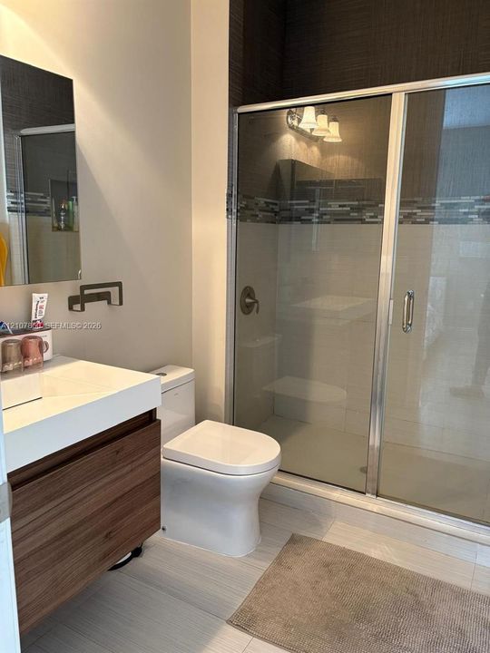 Floating vanity with wood-finish cabinetry, rectangular countertop basin, walk-in shower with glass enclosure, decorative tile inlay, and neutral tile flooring