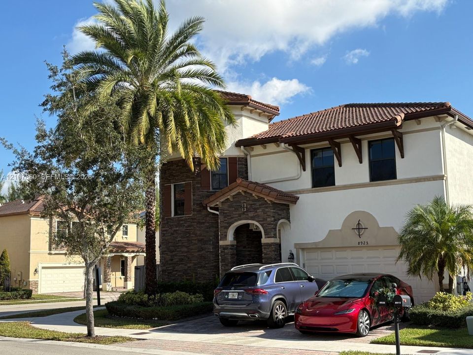Two-story exterior featuring light-toned stucco, decorative stone veneer, a tiled roof, and a paver driveway