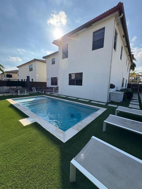 Rectangular swimming pool featuring stone coping, synthetic turf landscaping, and paved hardscaping