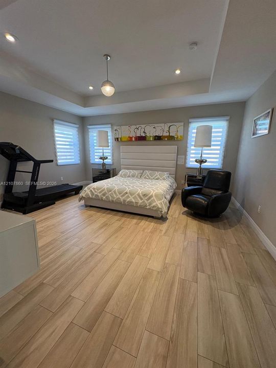 Spacious room featuring wood-finish flooring, recessed lighting, a tray ceiling, and windows fitted with roller shades