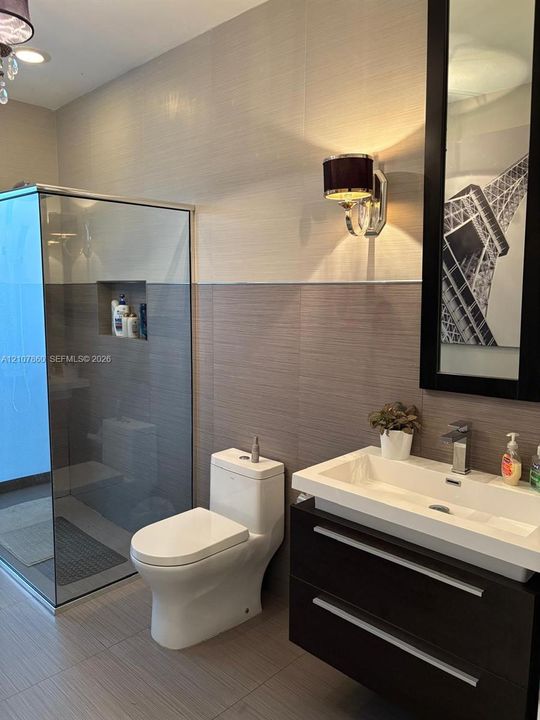 Floating vanity with rectangular vessel sink and chrome faucet, glass-enclosed shower featuring a recessed wall niche, two-tone textured wall tile, and wall-mounted drum shade sconce