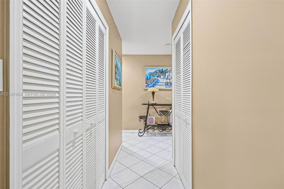 Hallway featuring white tiled flooring and dual white louvered closet doors