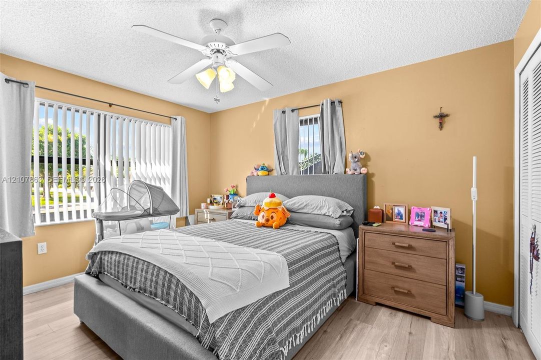 Bedroom featuring wood-finish flooring, a central ceiling fan with integrated lighting, dual-pane windows with vertical blinds, and louvered closet doors